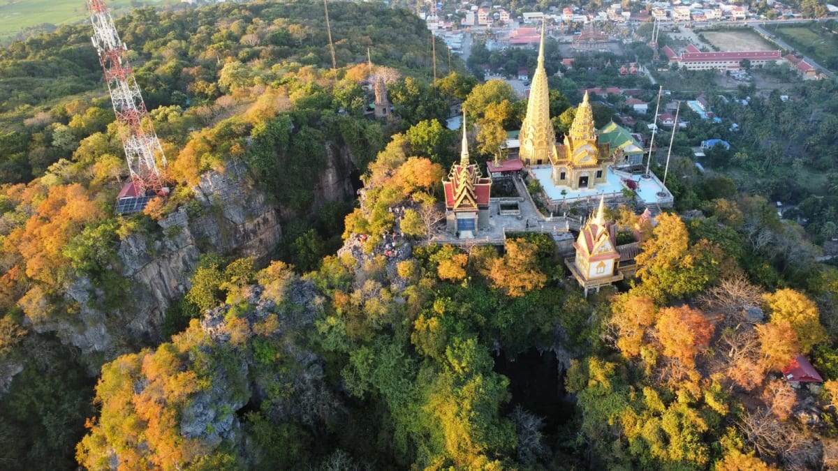 Vue aérienne d'une colline calcaire couronnée de pagodes aux flèches dorées, avec une bouche de grotte dans la roche, province de Battambang