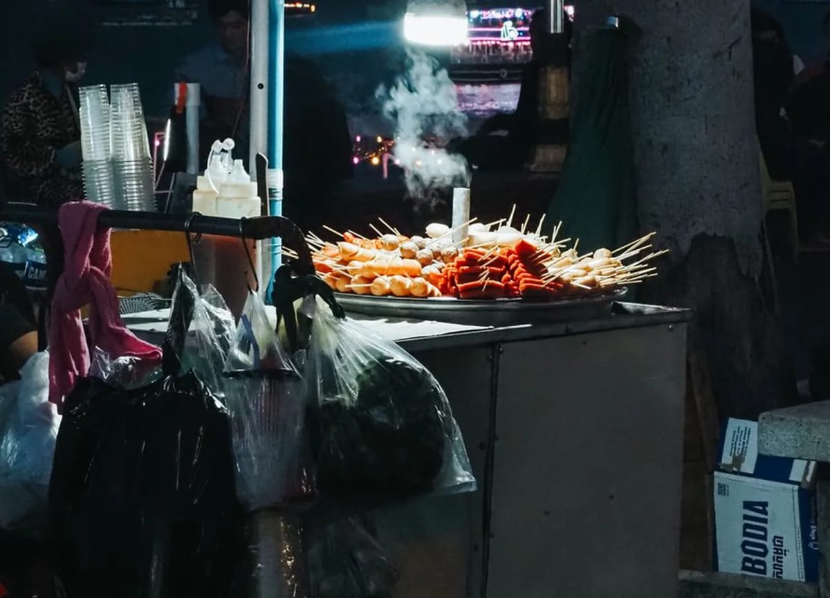 Charrette de cuisine de rue éclairée à l'ampoule le soir à Phnom Penh, avec des brochettes grillées sur un plateau