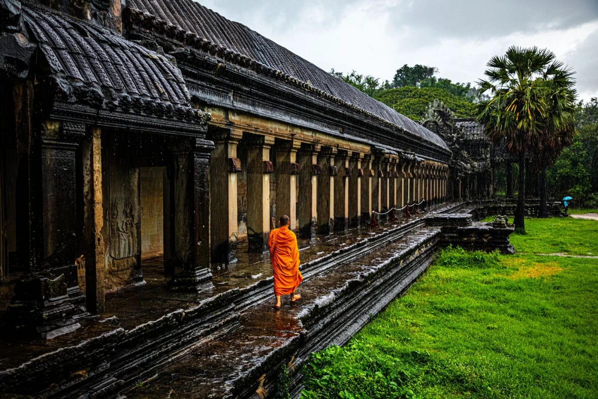 Moine en robe safran marchant le long d'une galerie d'Angkor Wat sous la pluie de mousson