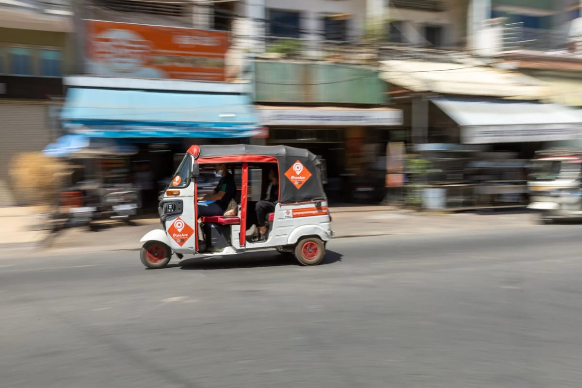 Tuk-tuk PassApp en mouvement dans une rue commerçante de Phnom Penh